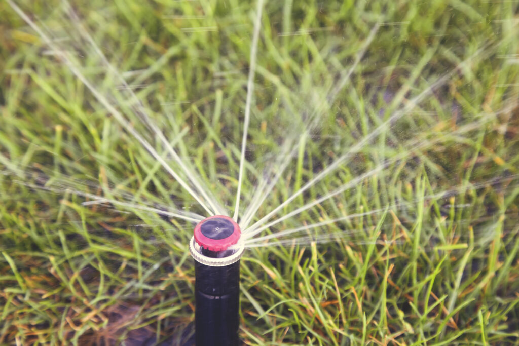 Automatic sprinkler head dispersing water on green grass, illustrating efficient irrigation for commercial landscapes in Little River, SC.