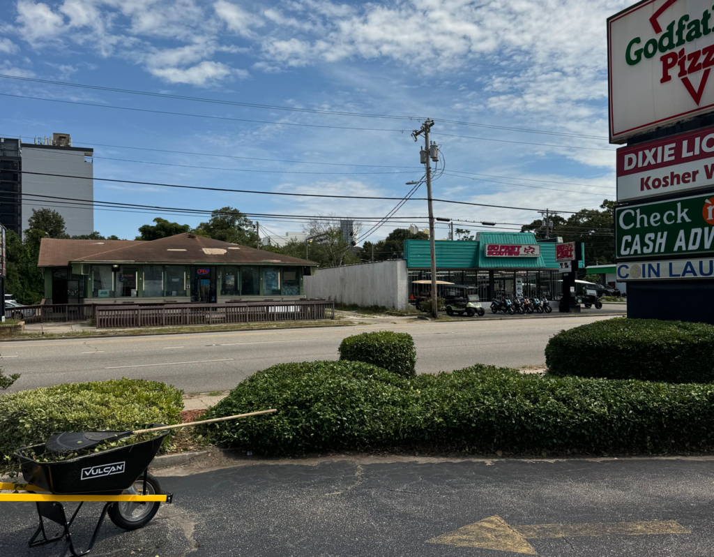 Wheelbarrow in foreground with "VULCAN" branding, commercial buildings and signage in background, including Godfather's Pizza, in North Myrtle Beach, SC.