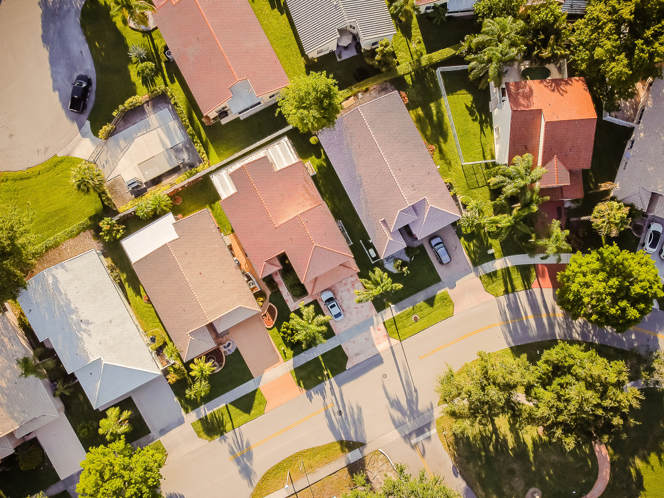 Aerial view of a well-maintained residential neighborhood with landscaped lawns, palm trees, and driveways, highlighting Coastal Breeze Landscaping's expertise in HOA property management and community landscaping services.
